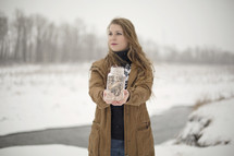a woman holding a mason jar full of fairy lights outdoors in the snow 
