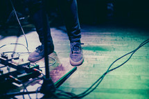 man on stage next to guitar foot pedals 