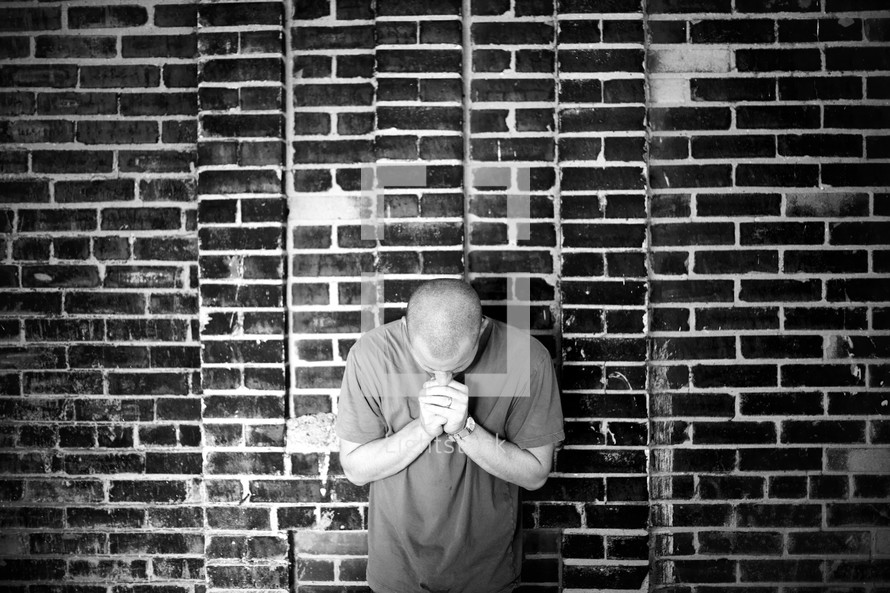 A man praying against a brick wall