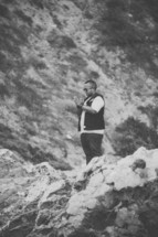Man standing on a rocky cliff praying.