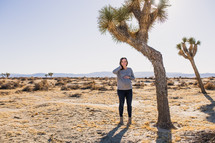 a woman standing in a desert under a tree