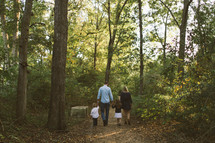a family walking through the woods along a trail holding hands 