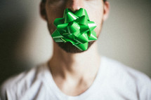 A man with a Christmas bow taped over his mouth