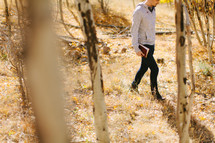 a man walking through a forest carrying a Bible 