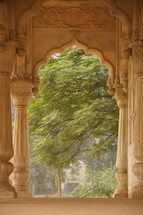 ornate archway with carved stone columns and large tree behind