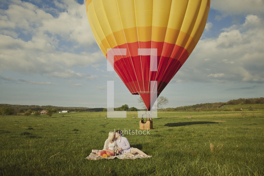 A couple kissing on a blanket with a hot air balloon in the background
