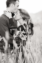 Man kissing woman forehead on a windy day outdoors in field of wheat love romance marriage engagement embrace