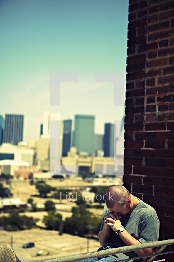 A white, young adult man praying on top of a building