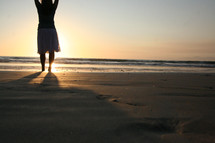 Woman standing on beach sand with raised hands