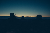 crescent moon, and silhouettes of rock formations against an evening sky 
