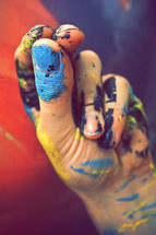 Man's hand colored with blue, yellow and black paint forming the Trinity symbol/sign with his fingers.