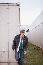 laughing man in a hat and jacket standing in front of a storage bin