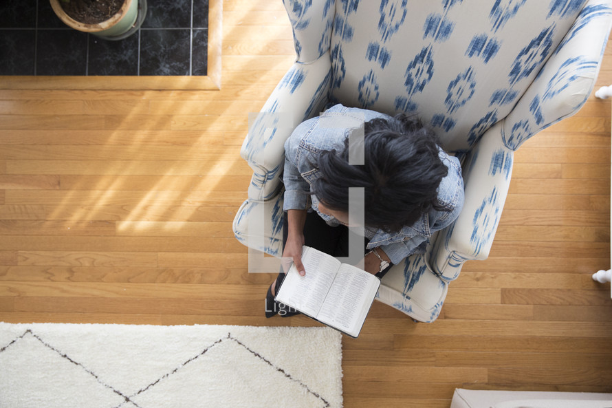 an African American woman sitting in a chair reading a Bible 
