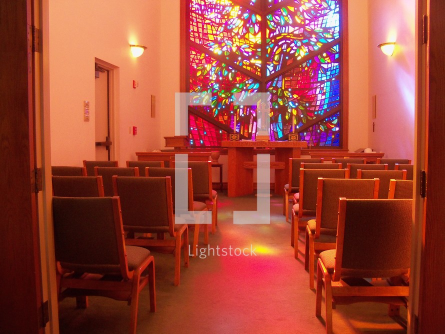 A colorful stained glass window lights up a prayer chapel with warm color and light to reflect peace, warmth, light and love.