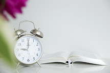 alarm clock and open Bible on a table 