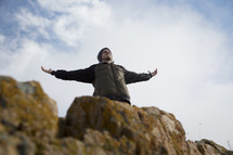 man standing on a mountainside with raised arms 