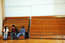 teens sitting on bleachers in a gymnasium 
