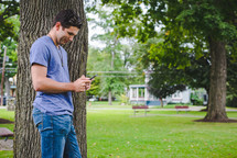 man standing beside a tree texting 