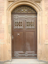 A decorative brown residence door in the middle of a town. 
