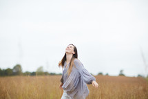 a young woman walking through a field with outstretched arms 