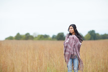 a woman standing in a field wrapped in a blanket 