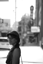 woman with a hat and purse standing on a sidewalk 