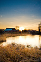 distant red barn across a farm pond