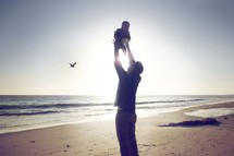 a father lifting up a baby on a beach 