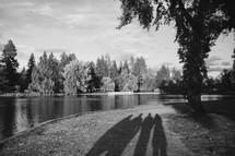 shadows on people standing on a pond shore 