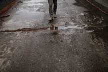 man in boots walking on a wet road 