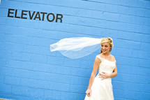 bride with her veil blowing in the wind standing in front of a blue wall