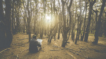 a man sitting on the forest floor reading a Bible 