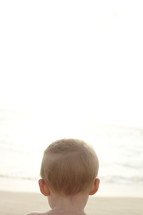 The back of a young boy's head looking out at the ocean