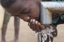 child drinking fresh water from a pipe of a new irrigation system