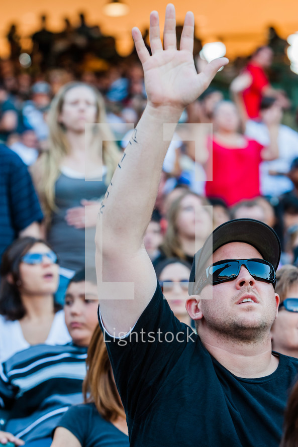 Man in sunglasses and baseball cap with right hand raised while looking to sky praise and worship
