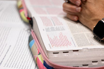 Close up of red Bible verses in Bible, with woman's hands folder in prayer over pages