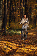 Young pretty woman riding vintage white bicycle in autumn park. Lady having fun on orange nature fall background. High quality photo