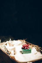 Green wrapped box with red bow lying on hay-filled basket.