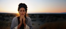 Portrait of a young woman praying in the desert at sunset with copy space