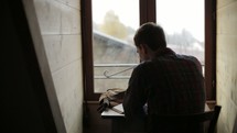 a man sitting at a desk in front of a window reading a Bible 