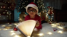 child amazed by magic book under Christmas tree 