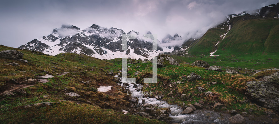 Panorama of snowy mountains and streams in spring