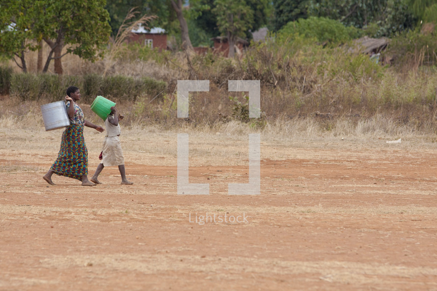 women carrying buckets down a dirt road