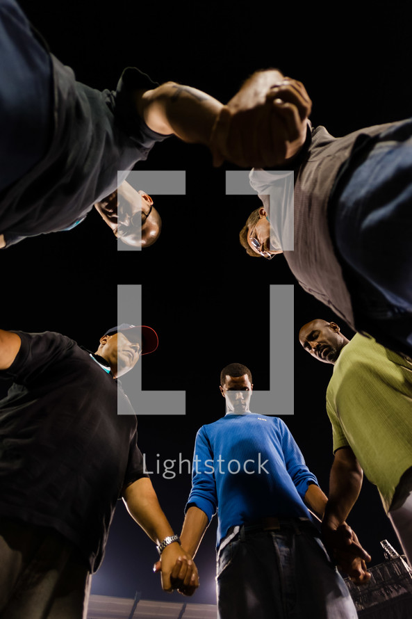 Men in prayer holding hands in a circle heads bowed 
