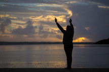 silhouette of a woman with raised hands on a beach 