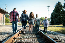 family walking holding hands on railroad tracks 