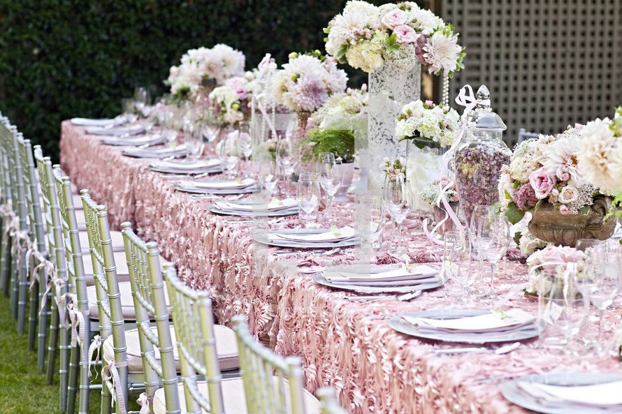 place setting on a set long table at a wedding reception, decor party event, silver chairs, pink linens flatware florals