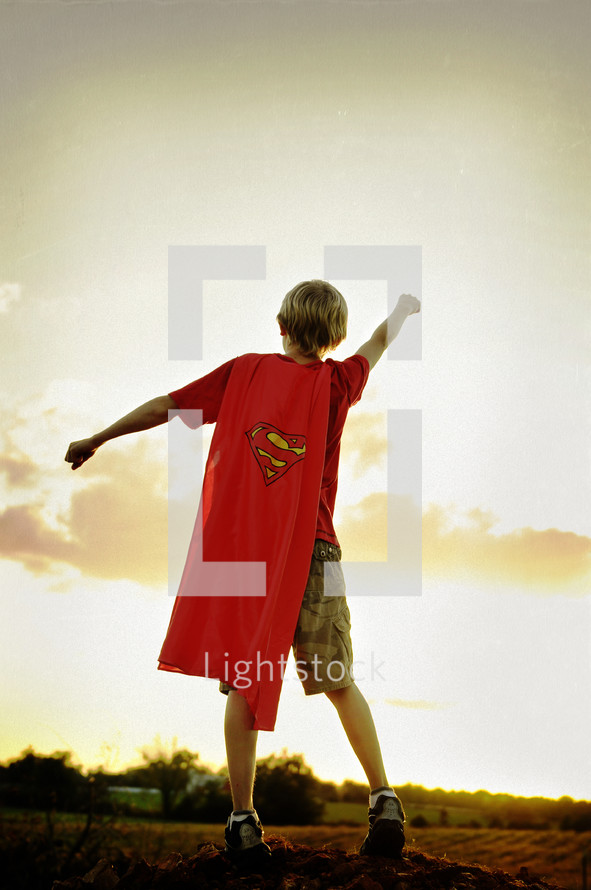 A boy in a superman cape with arms outstretched.