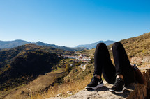a man relaxing lying down on a mountaintop with view of a village in the background 