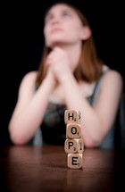 Bokeh view of a woman praying behind stacked block letters spelling hope.